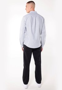 Chemise boutonnée rayée bleu et blanc à manches longues, avec un ourlet arrondi et un col ; associée à un pantalon noir et des baskets blanches.