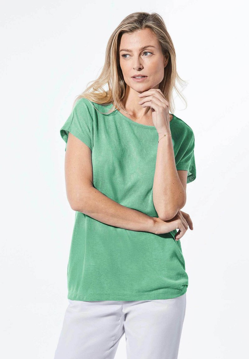 Grünes T-Shirt mit kurzen Ärmeln, lockerer Passform, weichem Material, rundem Halsausschnitt und glatter Oberfläche. Kombiniert mit weißen Hosen.