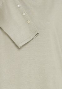 Hellgrünes Strickshirt mit kurzen Ärmeln. Verfügt über drei kleine, runde Knöpfe entlang der Schulter. Weicher, strukturierter Stoff.