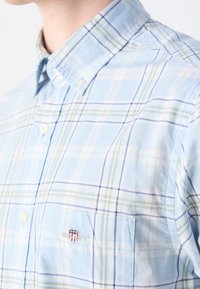 Camicia a quadri azzurro chiaro in cotone con colletto button-down. Presenta strisce bianche e verdi, tasca sul lato sinistro del petto con logo ricamato.