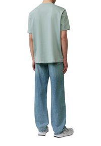 Lichtgroene katoenen t-shirt, korte mouwen, ronde halslijn, gecombineerd met losse blauwe denim jeans, zichtbare achterzak, gedragen met witte sneakers.