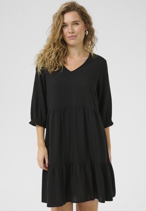 Robe noire mi-longue avec un décolleté en V, des manches trois-quarts, une jupe évasée et une texture de tissu douce. Détail froncé aux manches.
