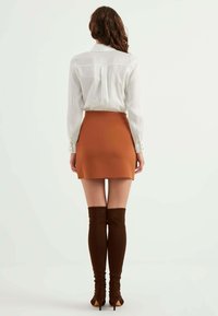 Witte lange mouwen blouse met een achterjuk, gecombineerd met een bruine minirok en bruine over-de-knie laarzen met een strakke pasvorm.