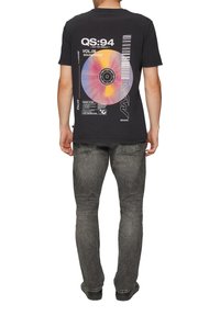 Zwarte T-shirt met een kleurrijke vinylplaat graphic met tekst. Gecombineerd met grijze jeans en zwarte schoenen. Eenvoudig, casual ontwerp.