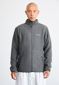 Graue Fleecejacke mit hohem Kragen, Frontreißverschluss und zwei Seitentaschen, mit einem dezenten Logo auf der oberen linken Brust.