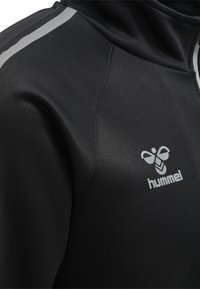 Svart atletisk hoodie i slät polyester med grå ränder och en liten logotyp. Har en figursydd design och mjuk känsla.