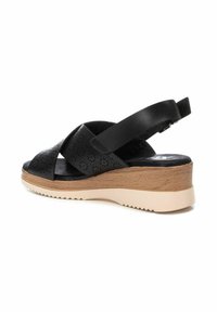 Sandalo wedge in pelle nera con tomaia perforata, design a cinturino incrociato, zeppa in legno testurizzato e suola in gomma leggera di colore crema.