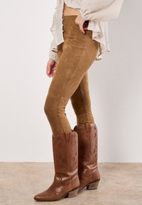 Tanfärgade faux suede leggings med en slät textur, som är kombinerade med bruna läder cowboystövlar med utskärningar och en klack i flera lager.