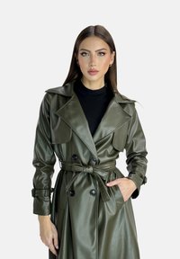 Kamouflagegrön trenchcoat i konstläder med dubbelknäppning framtill, stor krage, midjebälte och knäppta manschetter.