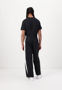 Svart t-shirt med korta ärmar och svarta träningsbyxor med vita sidostripar. Byxorna har ett elastiskt midjeband och dragsko. Vita sneakers.