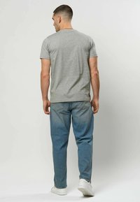 Grå bomull t-skjorte med korte ermer, sett bakfra, kombinert med lyseblå jeans og hvite joggesko. Enkel design, uten særpregede mønstre.