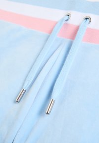 Világoskék melegítőnadrág fehér és rózsaszín vízszintes csíkokkal. Két kék cipzárhúzóval ezüst fém végződésekkel, puha anyagból készült.