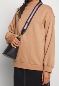 Borsa nera a forma di cono con chiusura dorata e tracolla a righe. Felpa marrone con maniche lunghe, polsini a coste e dettaglio di collo alto.