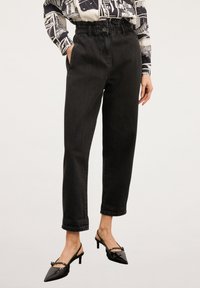 Svarta denimbyxor med hög midja, elastisk midjeband och sidofickor; matchade med glansiga svarta kitten-heel skor.