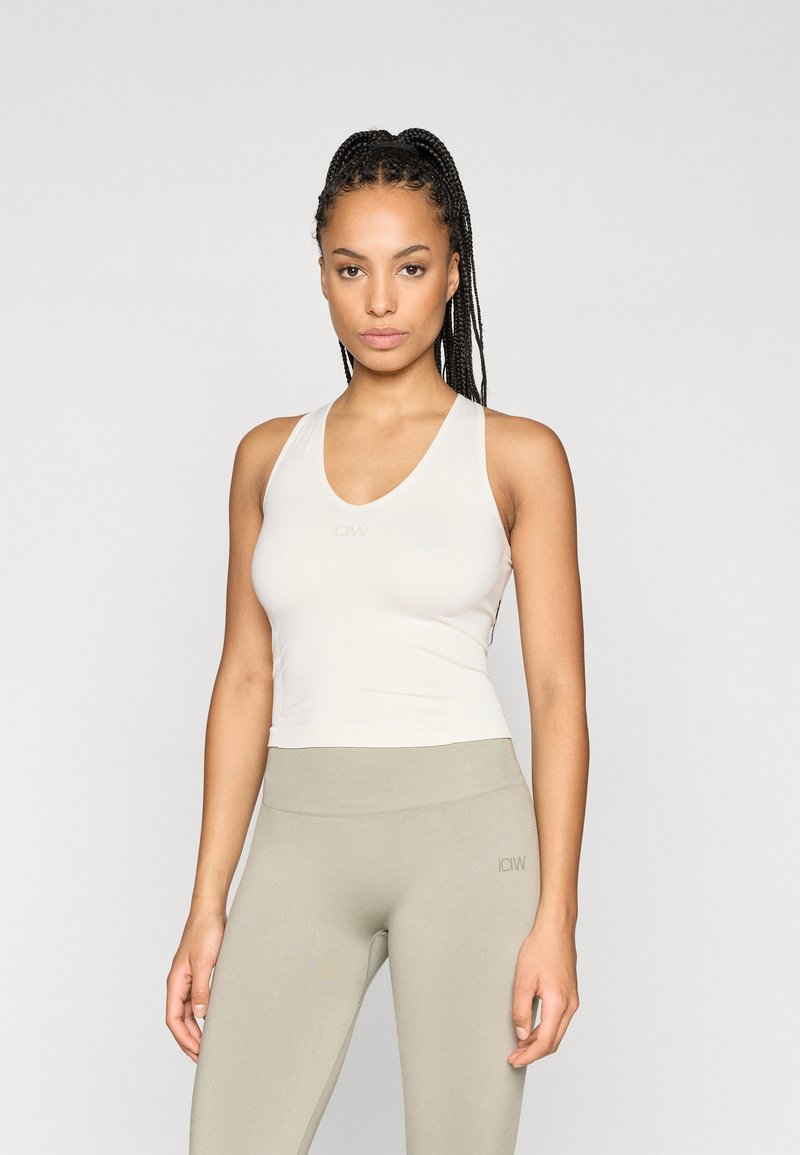 Ανοιχτό μπεζ αθλητικό τοπ με σχέδιο V. Φτιαγμένο από απαλή υφή, εφαρμοστό στυλ, συνδυασμένο με ανοιχτό πράσινες κολάν. Διακριτική λεπτομέρεια λογότυπου.