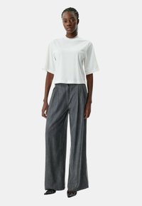 Wit cropped t-shirt met korte mouwen, gecombineerd met grijze wijde broek met plooien. De outfit heeft een relaxte maar gestructureerde uitstraling.