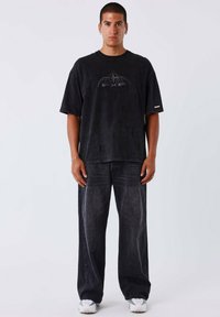 Zwarte oversized T-shirt met een logodesign, gecombineerd met donker gewassen baggy jeans en witte sneakers. Eenvoudige, casual streetwear uitstraling.