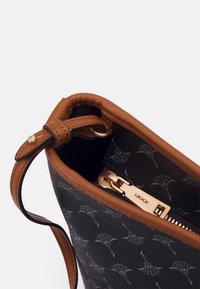 Musta nahkainen käsilaukku ruskeilla yksityiskohdilla, jossa on vetoketjusuljenta ja sisäpuolella kuvioitu vuori. Metallinen vetoketju, jossa näkyvissä logo.