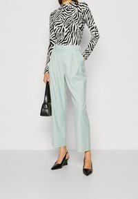 Zwart-wit zebra print lange mouwen top, lichtgroene brede broek, zwarte handtas en puntige sleehakken.