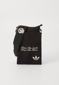 Svart stoff skulderveske med glidelås, brodert tekst og en hvit Adidas-logo. Har en justerbar stropp og metalldetaljer.