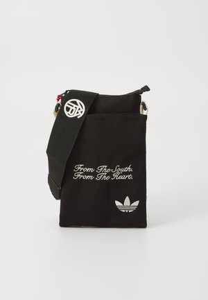 Svart stoff skulderveske med glidelås, brodert tekst og en hvit Adidas-logo. Har en justerbar stropp og metalldetaljer.