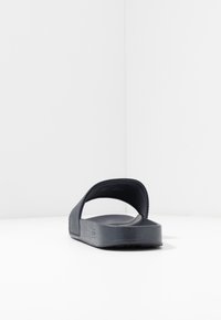 Svart slip-on sandal i texturerad gummi, med öppen häl, bred rem och en minimalistisk design med subtila detaljer.