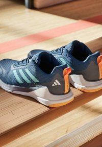 Scarpe sportive blu con tomaia testurizzata, strisce verdi, dettagli arancioni e una suola bianca. Presentano una linguetta per una facile indossabilità.