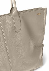 Beige læder tote taske med en struktureret finish, der har to håndtag og lynlås-lukning. Guldpræget logo på siden.