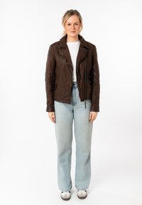 Chaqueta de motorista de cuero marrón con estampado de leopardo, cremallera asimétrica y solapas con muescas; combinada con jeans rectos de pierna ligera en azul claro y zapatillas.