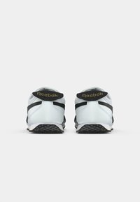 O pereche de adidași Reebok alb-negru, vizualizați din spate pe un fundal alb, evidențiind logo-ul mărcii și designul călcâiului.