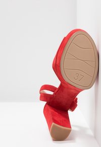 Sandale à talons hauts en daim rouge avec bride de cheville, taille 37, présentée par la semelle sur fond blanc.