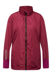 Kevyt takki syvänpunaisena, jossa on suuri kaulus, täysi vetskari etuosa, kontrastiväri purppurat käsivarsissa ja rei'itetyt paneelit ilmanvaihtoa varten.