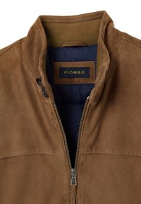 Braune Wildlederjacke mit hohem Kragen, Reißverschluss und gerippten Strickeinsätzen. Mit marineblauem Stoff gefüttert. Markenetikett innen sichtbar.