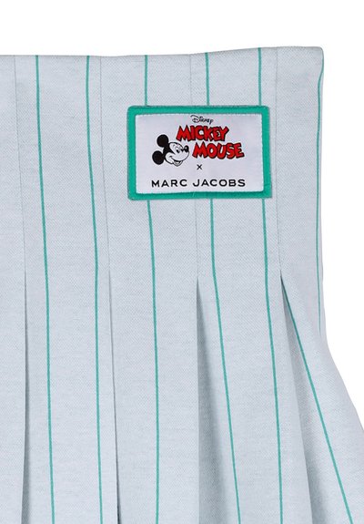 Tessuto bianco con strisce verdi verticali, una toppa che mostra il volto di Topolino e testo rosso e nero con la scritta "Disney Topolino x Marc Jacobs."