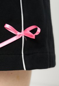 Tissu noir avec une rayure verticale blanche et un petit ruban en satin rose noué près de l'ourlet, sur fond de peau claire.