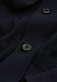 Cárdigan de punto en azul marino oscuro con una textura suave, un diseño clásico y un botón negro brillante con un detalle de cuatro agujeros.