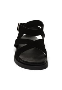 Sandalo nero con cinturini incrociati in morbido suede, punta rotonda e suola piatta con finitura liscia. Dettaglio della fibbia regolabile.