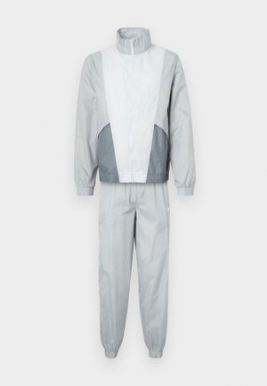 Ensemble Nike en gris clair avec des accents gris plus foncé. Comprend une veste zippée avec un col haut et des poignets élastiqués, ainsi que des pantalons assortis.