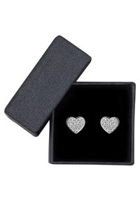 Silver hjärtformade örhängen, prydda med små klara stenar, placerade i en texturerad svart låda med en mjuk svart inredning.