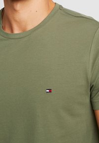 T-shirt olive green a maniche corte realizzata in morbido cotone, con un piccolo logo in rosso, bianco e blu sulla parte sinistra del petto.