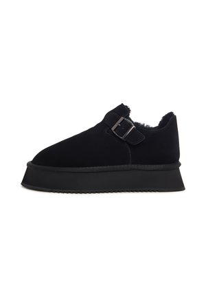 Zwarte suède schoenen met een ronde vorm, een zijgespsluiting, een textuurvoering en een dikke zwarte rubberen zool.
