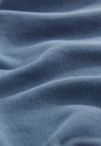 Katoenen breisels in een zachte, mediumblauwe kleur, met een gladde textuur, subtiele ribbelpatroon en zachte drapering.