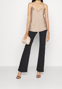 Camiseta de satén beige con tirantes finos, combinada con pantalones acampanados negros. La modelo sostiene un clutch dorado con estampado y lleva sandalias de tacón negras.