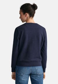 Felpa blu navy con scollatura rotonda, polsini e orlo a costine. Texture morbida, design minimalista, con un sottile dettaglio di cucitura sul retro.