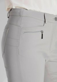 Lichtgrijze broek met een aansluitend ontwerp, een gladde textuur en een ritszak aan de zijkant. Stiksel is zichtbaar langs de naden.