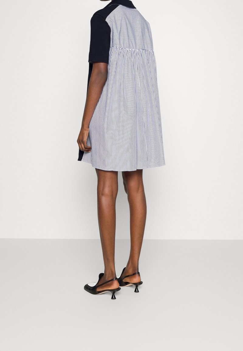 Femme portant une robe ample à manches courtes avec des rayures verticales dans le dos, associée à des chaussures à talons kitten slingbacks noires et blanches.