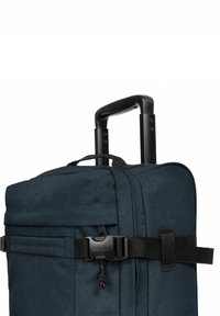 Tummansininen pehmeämatkakassi, jossa on vedettävä musta kahva, sivuhihnalla suljettava ja tekstuurihohtoinen kangaspinta.