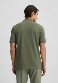 Olivgrünes Poloshirt mit kurzen Ärmeln, klassischem Kragen und entspannter Passform. Glatte Textur, dezente Nahtdetails und Rückansicht.