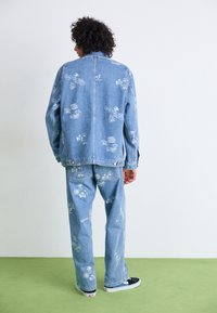 Light blue denim jacket and matching pants with white printed graphics. Casual fit, button closure, and contrasting stitching details.