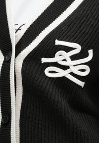 Czarny prążkowany sweter rozpinany z białą lamówką i guzikami, z białym haftowanym abstrakcyjnym logo na piersi.